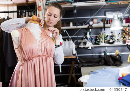 Woman professional sewer measuring dress at mannequin workshop Woman professional sewer measuring dress at mannequin workshop 64350547