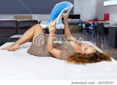 Portrait of attractive girl lying on bed while testing quality of new mattress in salon Portrait of attractive girl lying on bed while testing quality of new mattress in salon 64350557