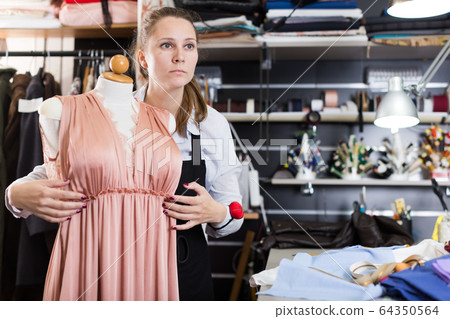 Woman standing near dress at mannequin in sewing workshop Woman standing near dress at mannequin in sewing workshop 64350564