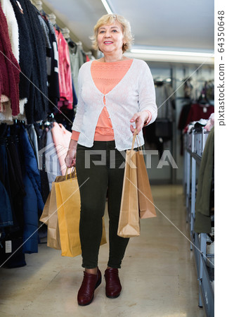 Woman consumer in the dress boutique among clothes with paper bags Woman consumer in the dress boutique among clothes with paper bags 64350648