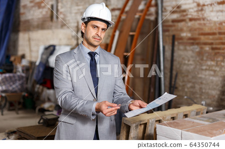Unhappy man holding paper at construction site Unhappy man holding paper at construction site 64350744