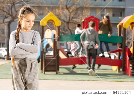 Upset little girl standing on playground 64351104