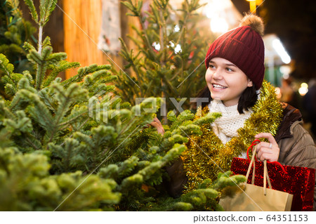 Girl staying at market among Christmas trees Girl staying at market among Christmas trees 64351153