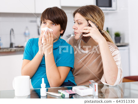 Mother calling doctor, son sneezing Mother calling doctor, son sneezing 64351330