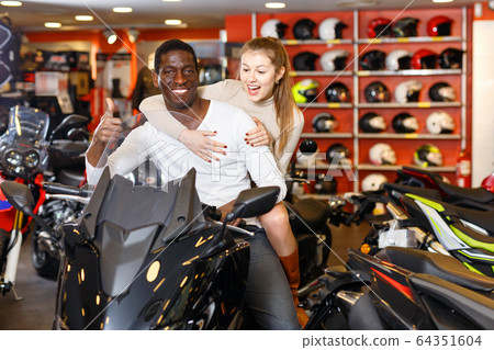 Happy young couple satisfied with choice in modern motorcycle salon Happy young couple satisfied with choice in modern motorcycle salon 64351604