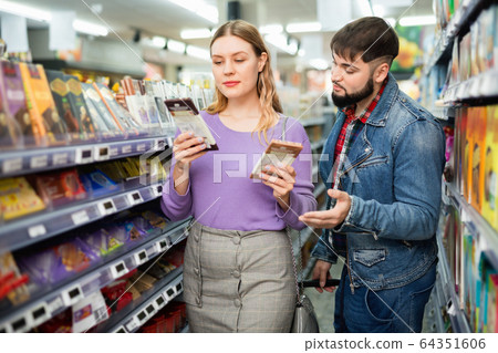 Happy young couple looking for sweet chocolate in grocery store Happy young couple looking for sweet chocolate in grocery store 64351606