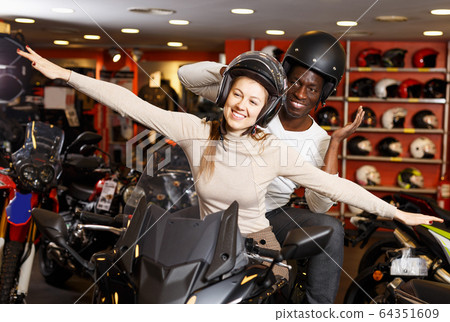 Couple sitting together on new motorcycle in store and having fun Couple sitting together on new motorcycle in store and having fun 64351609
