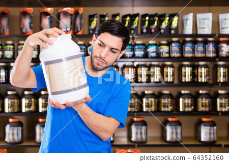 Serious young muscular man choosing sport nutrition products in shop 64352160
