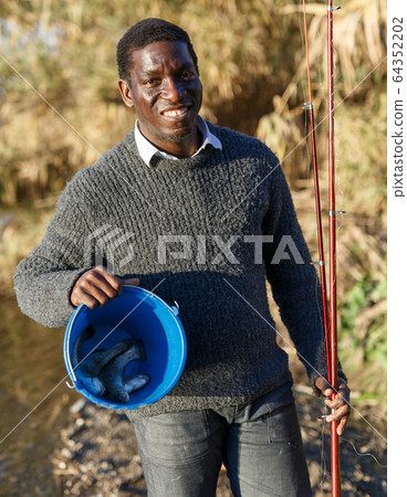 Fisherman holding rod and bucket 64352202