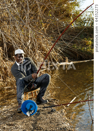 Fisherman sitting on stool and pulling fish Fisherman sitting on stool and pulling fish 64352273