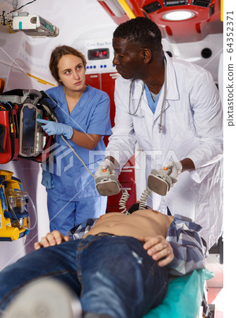 Doctor resuscitating patient with help of defibrillator Doctor resuscitating patient with help of defibrillator 64352371