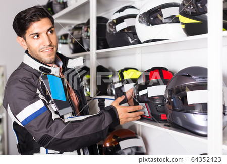 Man in moto jacket is choosing new helmet for motorbike in the store. 64352423