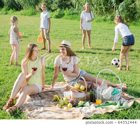 Smiling females on picnic in sunny park with happy kids Smiling females on picnic in sunny park with happy kids 64352444