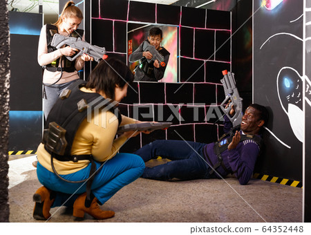 Modern people of different nationalities with laser pistols playing laser tag on dark labyrinth Modern people of different nationalities with laser pistols playing laser tag on dark labyrinth 64352448