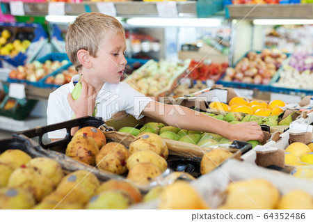 little boy choosing fresh fruits at shop 64352486