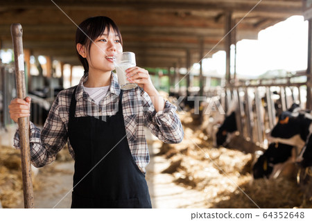 Young positive female dairy farm worker standing with glass of fresh milk 64352648
