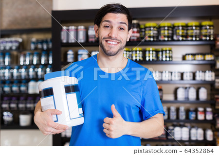 Smiling sportman holding thumbs up in shop of sport nutrition Smiling sportman holding thumbs up in shop of sport nutrition 64352864