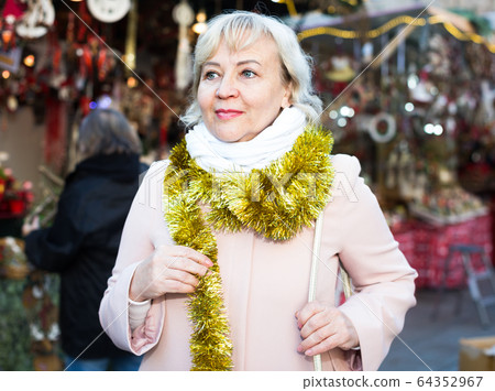 Positive female in tinsel on Christmas fair 64352967