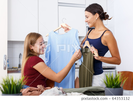Two young positive girlfriends looking new clothes at table and sharing 64353132
