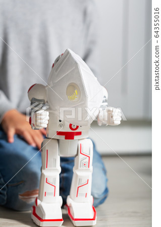 Boy plays with his toys, such as coronavirus protection mask and robot 64355016