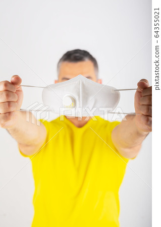 A man in yellow t-shirt holds medical mask. Coronavirus concept. Protect your health. A man in yellow t-shirt holds medical mask. Coronavirus concept. Protect your health. 64355021