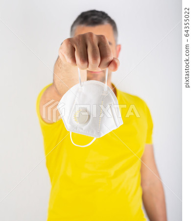 A man in yellow t-shirt holds medical mask. Coronavirus concept. Protect your health. A man in yellow t-shirt holds medical mask. Coronavirus concept. Protect your health. 64355022