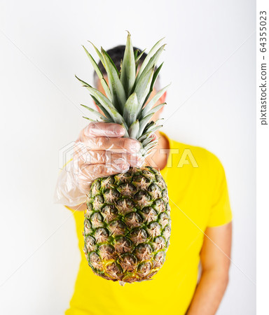 A man in yellow t-shirt wears supermarket gloves and holds ananas. Safety buying A man in yellow t-shirt wears supermarket gloves and holds ananas. Safety buying 64355023
