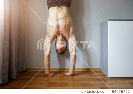 Young man standing in handstand at home Young man standing in handstand at home 64356762