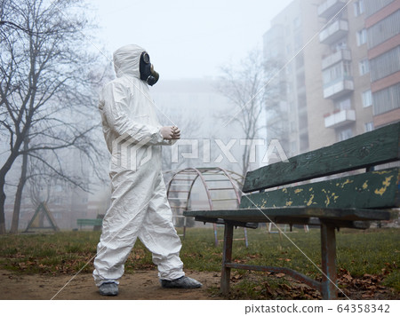 Scientist in gas mask and protective clothing standing outdoors. 64358342