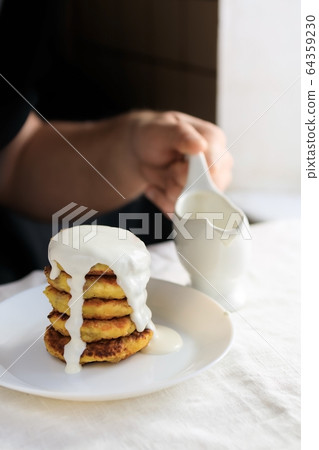 A circumcised man in a black T-shirt holds a white gravy boat in his hands and pours the curd 64359230