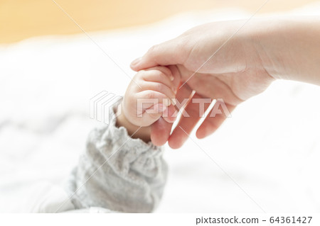 Mothers hand holding baby hand in bright room 64361427
