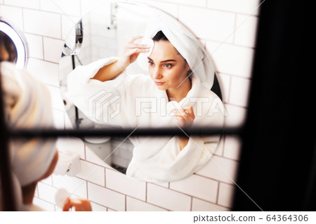 Pretty woman doing cosmetic procedures to care for face skin in bathroom 64364306