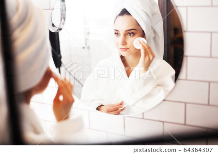 Pretty woman doing cosmetic procedures to care for face skin in bathroom 64364307