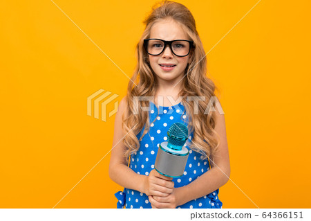 A little girl with glasses with a microphone is interviewed, the picture is isolated on yellow A little girl with glasses with a microphone is interviewed, the picture is isolated on yellow 64366151