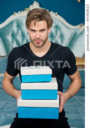 Man with present boxes sit on bed in bedroom Man with present boxes sit on bed in bedroom 64368615