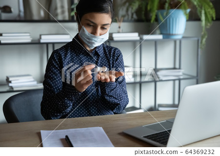 Young Indian woman in face mask cleanse hands with sanitizer 64369232