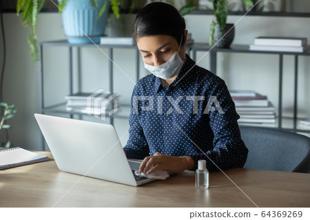 Female employee in face mask disinfect computer at workplace 64369269