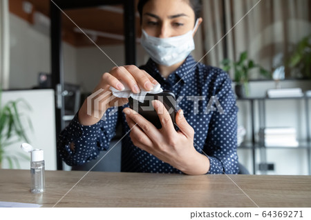 Female employee disinfect cellphone with sanitizer at workplace Female employee disinfect cellphone with sanitizer at workplace 64369271