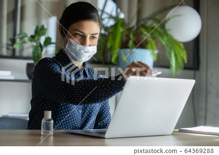 Female employee in face mask disinfect laptop with sanitizer 64369288