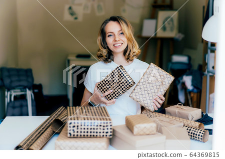 A young woman holds wrapped gifts and smiles 64369815