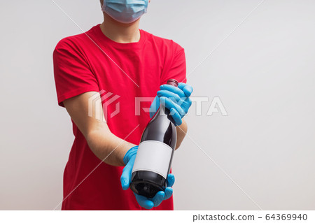 Delivery man wearing protective gloves and mask holding a bottle of wine Delivery man wearing protective gloves and mask holding a bottle of wine 64369940