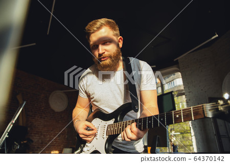 Caucasian musician playing guitar during online concert at home isolated and quarantined, impressive improvising in sunlight 64370142