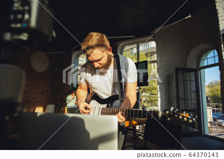 Caucasian musician playing guitar during online concert at home isolated and quarantined, impressive improvising in sunlight 64370143