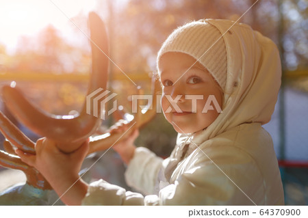 Cute girl riding a carousel holding deer horns 64370900