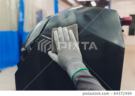 Auto mechanic preparing the car for paint job by applying polish with the power buffer machine Auto mechanic preparing the car for paint job by applying polish with the power buffer machine 64372494