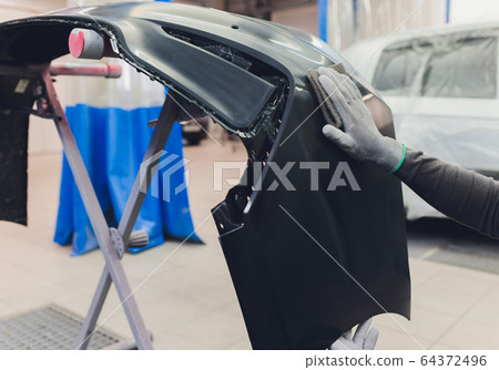 Auto mechanic preparing the car for paint job by applying polish with the power buffer machine 64372496