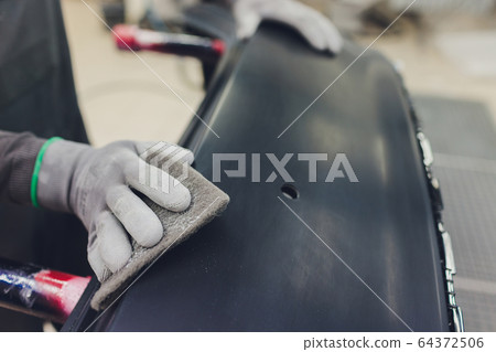 Auto mechanic preparing the car for paint job by applying polish with the power buffer machine Auto mechanic preparing the car for paint job by applying polish with the power buffer machine 64372506