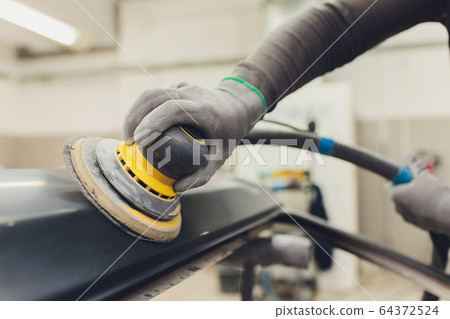 Auto mechanic preparing the car for paint job by applying polish with the power buffer machine Auto mechanic preparing the car for paint job by applying polish with the power buffer machine 64372524