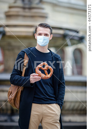Beautiful young man holding pretzel and relaxing in park Beautiful young man holding pretzel and relaxing in park 64373371