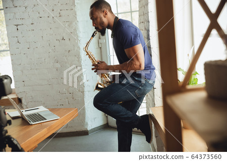 African-american musician playing saxophone during online concert at home isolated and quarantined, impressive improvising 64373560